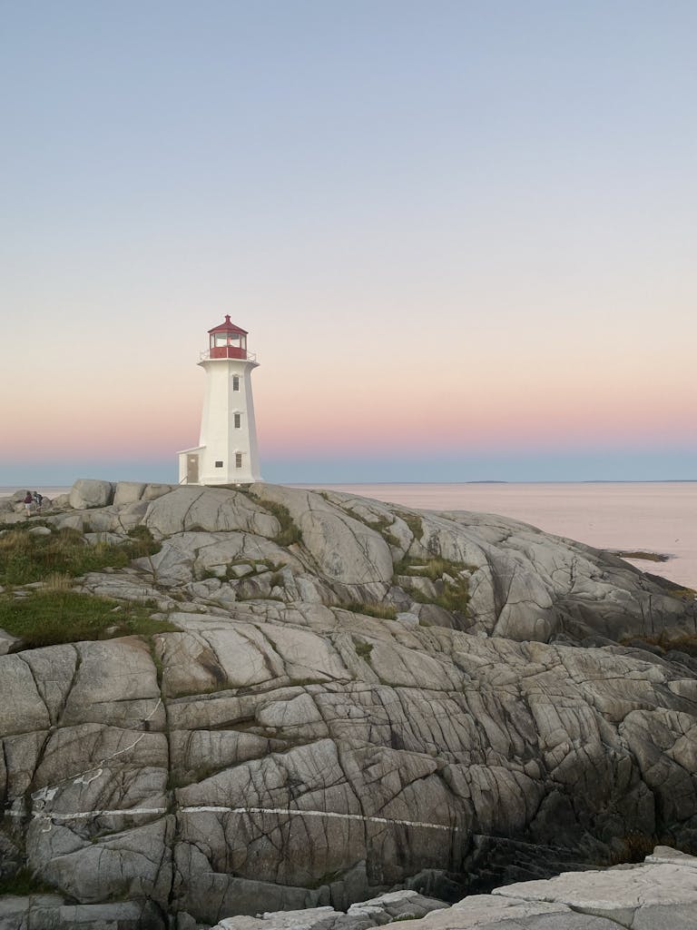 A serene view of a lighthouse with pastel skies on a rocky coastline during twilight.