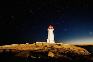 Captivating night view of Peggy’s Point Lighthouse under a starry sky in Canada.